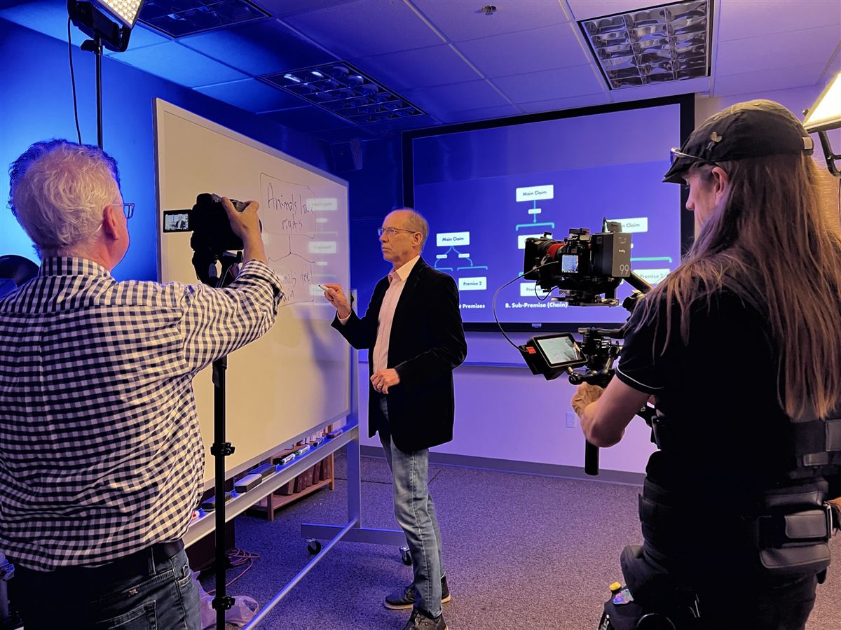Gary Comstock at a whiteboard while a film crew records a Thinker lesson